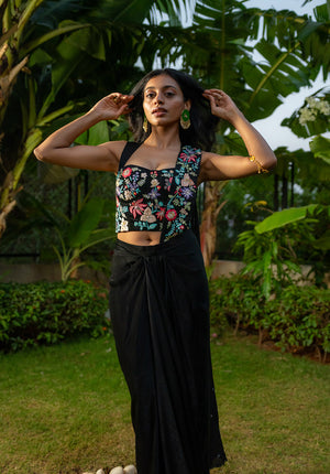 Model wearing solid black saree fusion set with embellished blouse and draped saree.