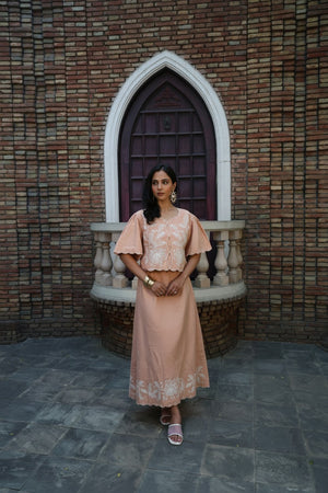 Model wearing fawn coord set with white embroidery and scalloped hem sitting outdoors