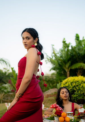 Model standing near a garden table, displaying the elegant and flexible fit of the red dress in a graceful pose.