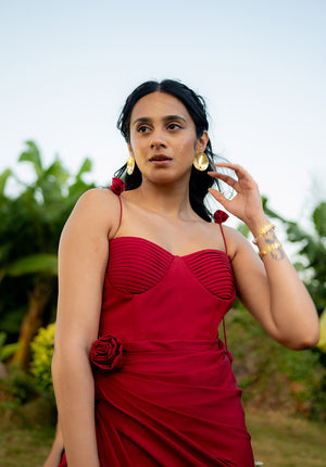 Model standing in a garden wearing a red dress styled with gold earrings, capturing a chic and serene outdoor look.