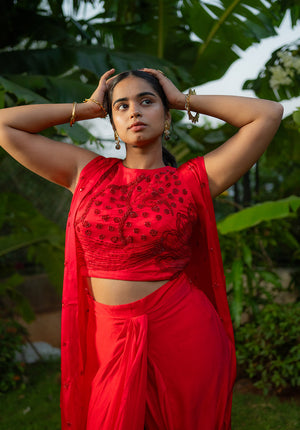 Coordinated red lehenga set featuring matching blouse, skirt, and sheer cape for a graceful appearance.