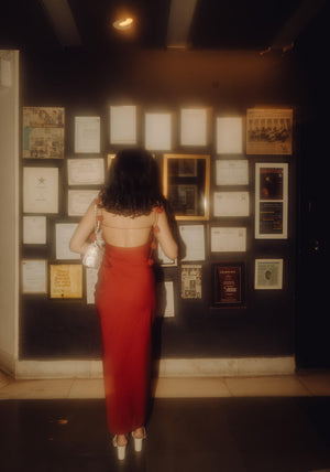 Back view of the red midi dress as the model stands near a board decorated with photos, highlighting the dress’s flattering silhouette.