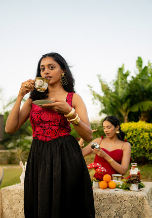 Model in a rose-embroidered black and red bustier dress sipping tea, styled with gold jewellery