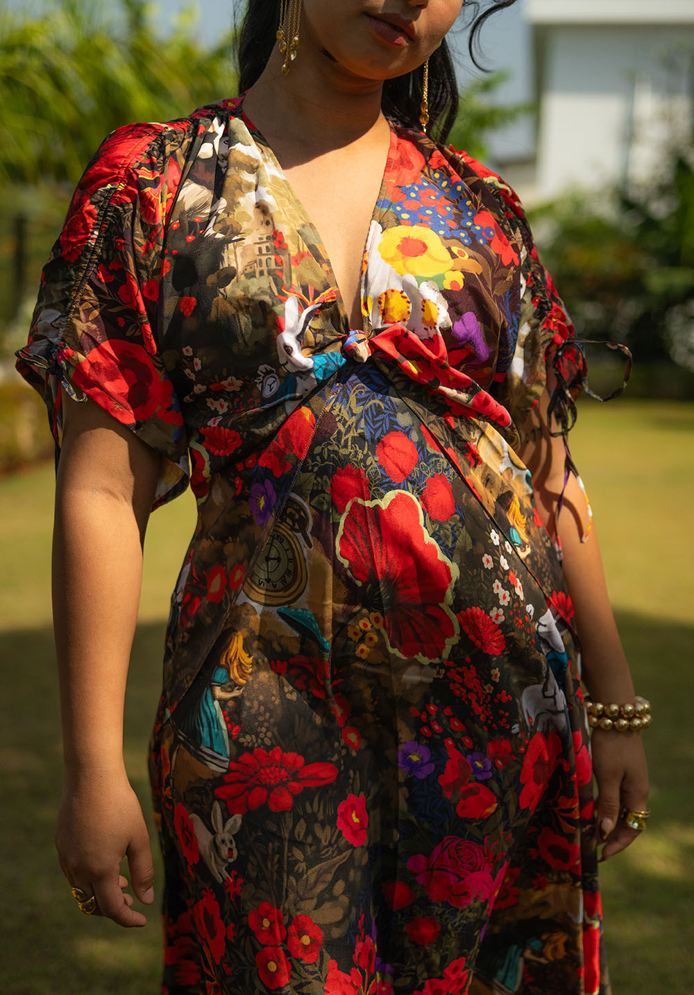 Close-up of a floral dress with V neckline, short sleeves, knot effect at the bust, and golden bangles