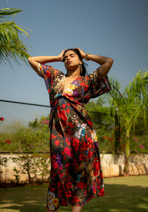 Model standing in a garden wearing a calf-length floral dress with a relaxed silhouette, captured in a full-body pose