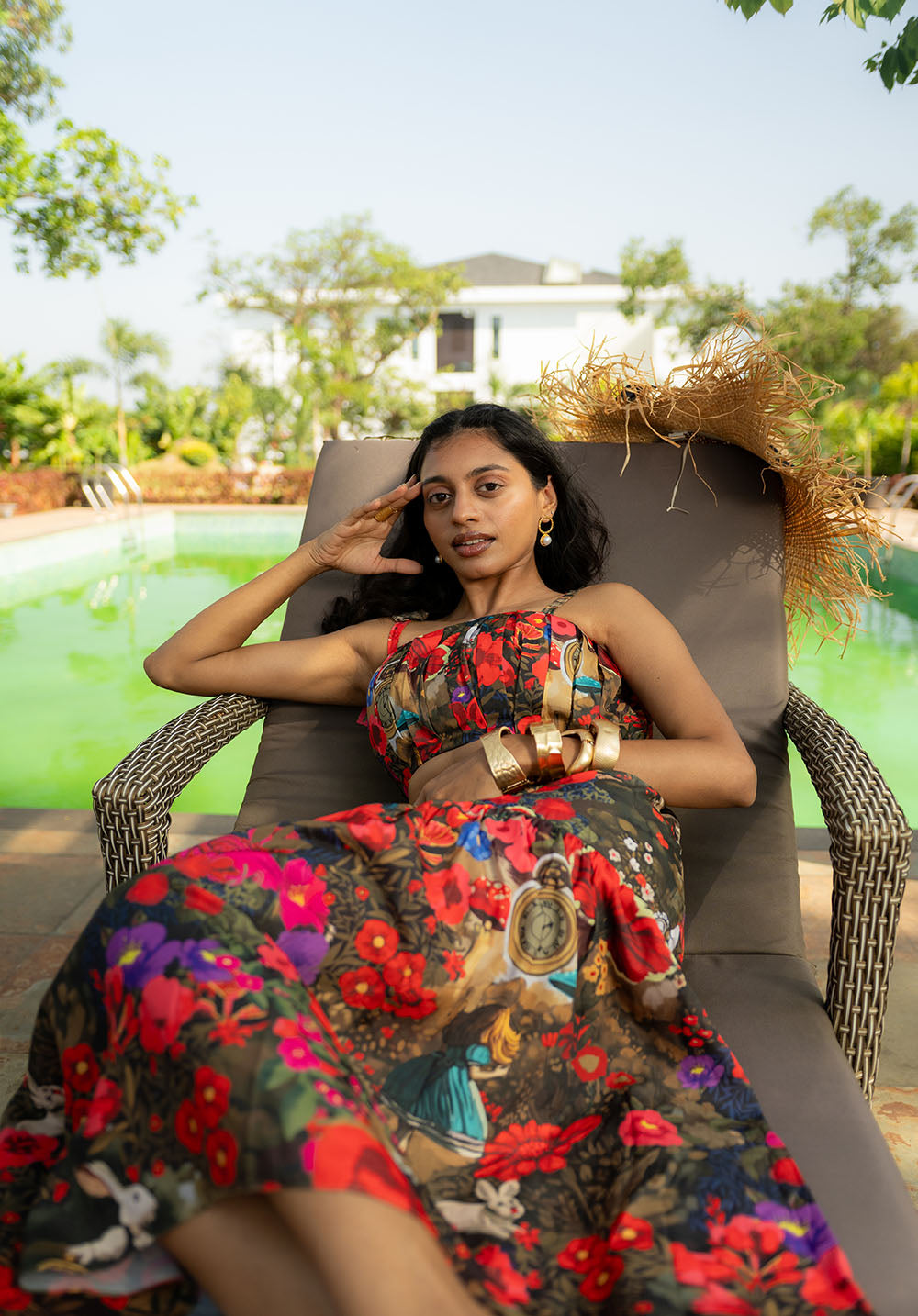 Model sitting on a chair in a floral long skirt and top, wearing golden bangles