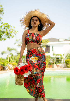 Model standing poolside wearing a floral co-ord set, cap, and holding a flower bag
