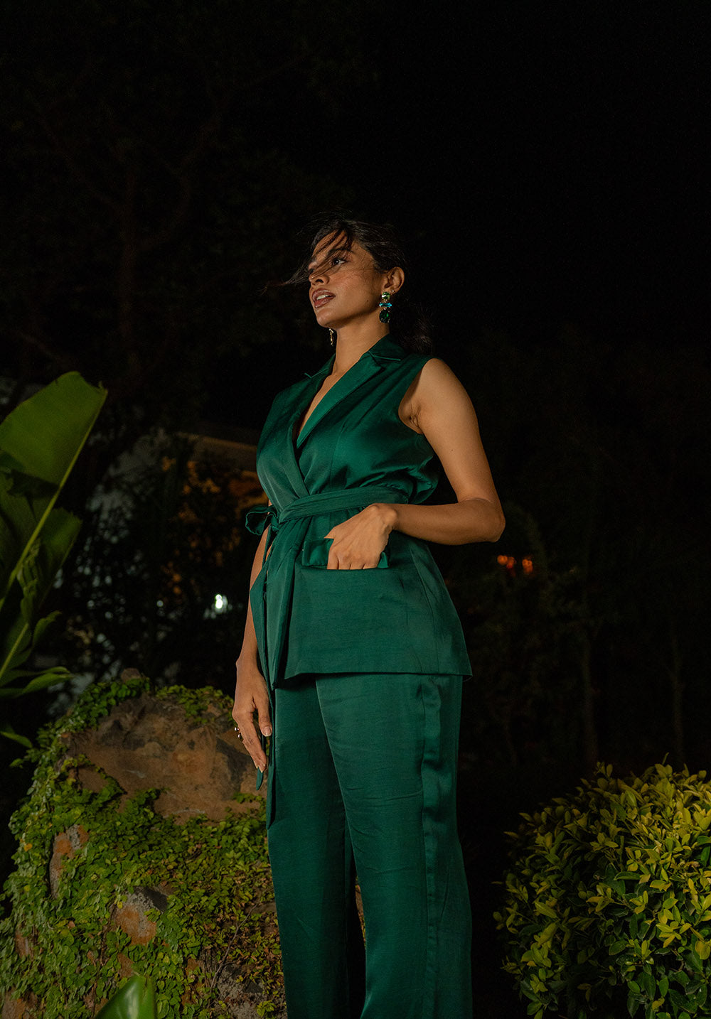 Side pose of model wearing a wrap-tie jacket in green during a night scene