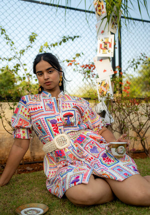Model sitting on the floor in a puff-sleeve dress, holding a vintage-style cup in her hand