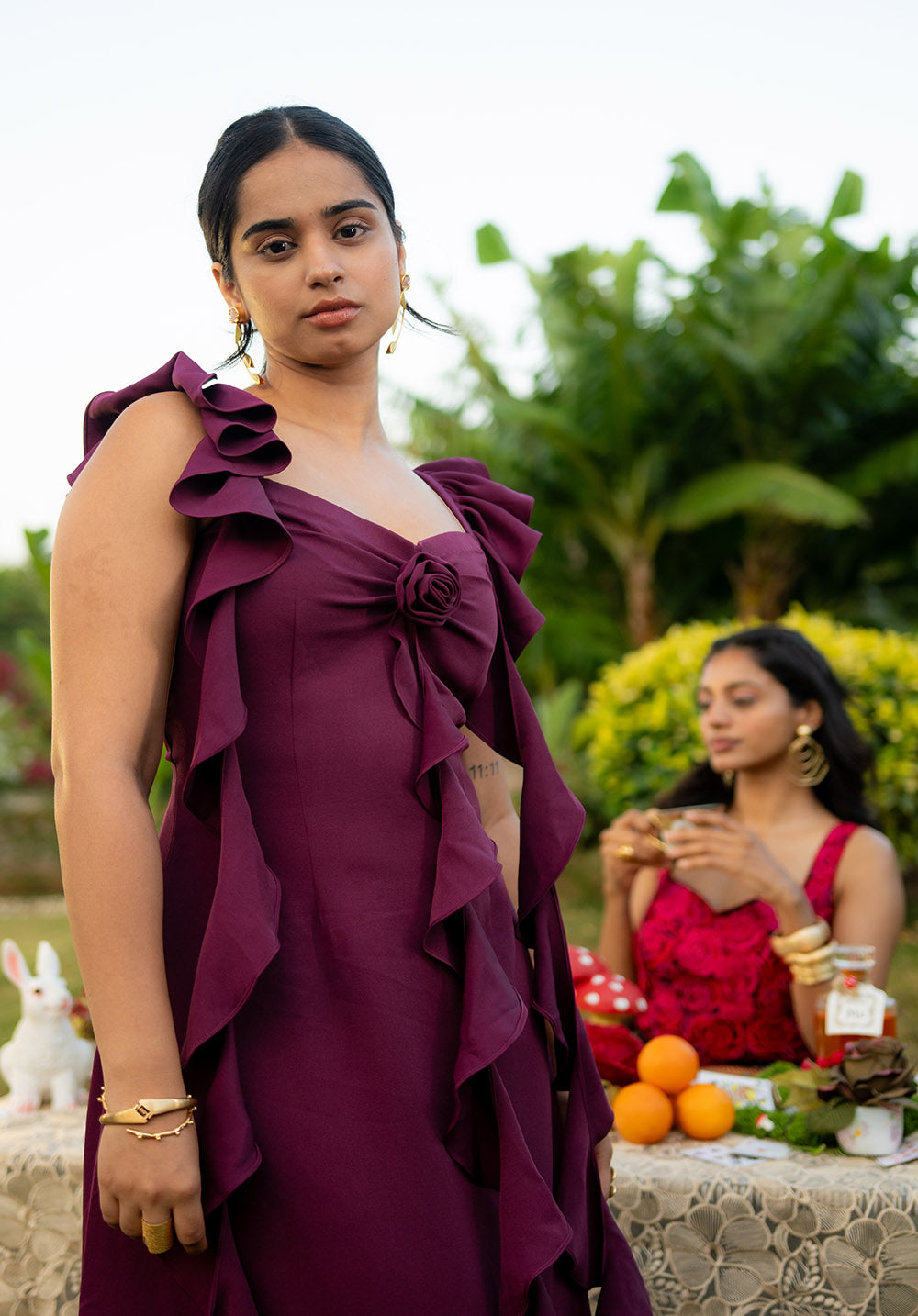 Model standing near a table wearing a sleeveless dress styled with a golden bangle