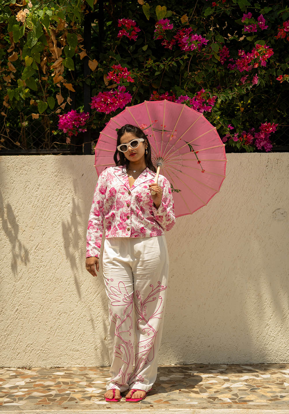 Model holding an umbrella, wearing a pink printed blazer with white pants