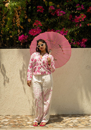 Model holding an umbrella, wearing a pink printed blazer with white pants
