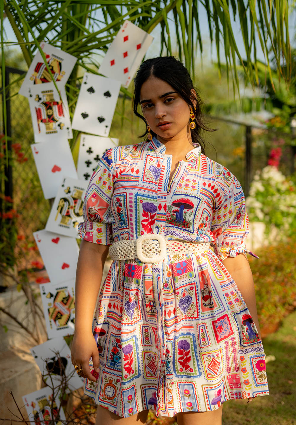 Model standing in a white dress with multicolour prints and a belt, with cards visible in the background