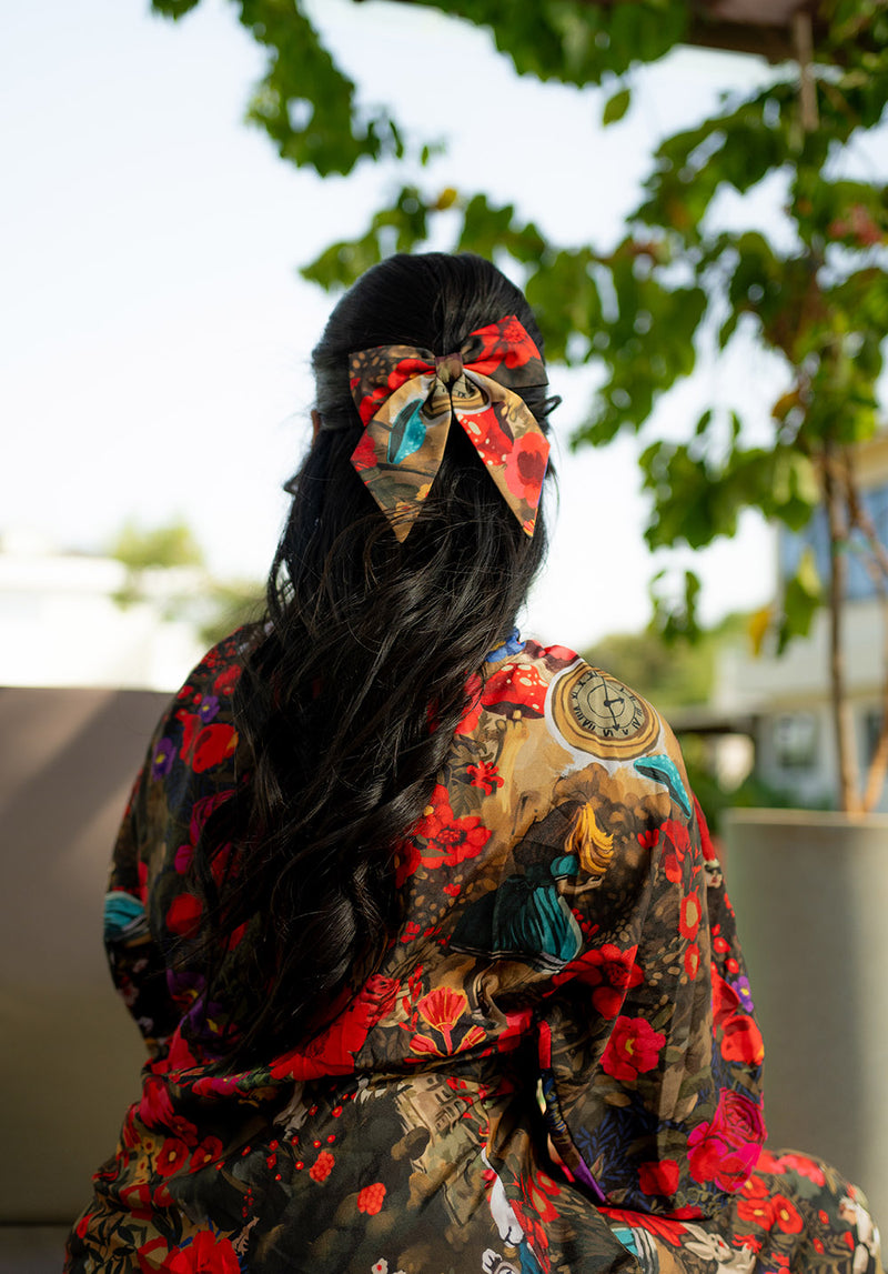 Back view of a seated model wearing a green dress with long hair styled in matching bows

