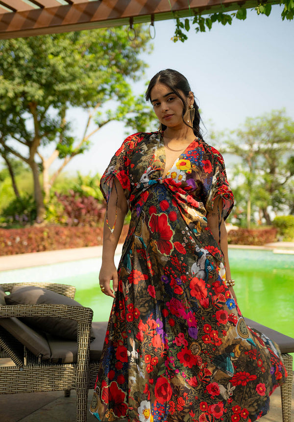 Woman standing in a garden near a chair wearing a short-sleeved floral dress with V neckline and drawstring detail
