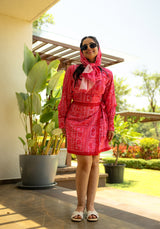 Model standing in a short printed dress, wearing a matching scarf and sunglasses