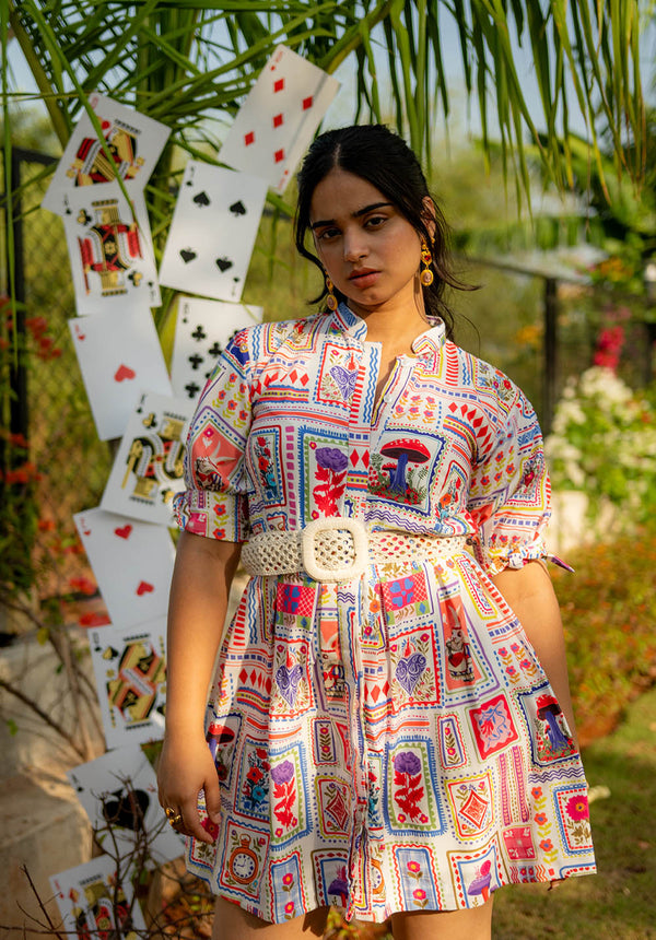 Model standing in a white dress with multicolour prints and a belt, with cards visible in the background
